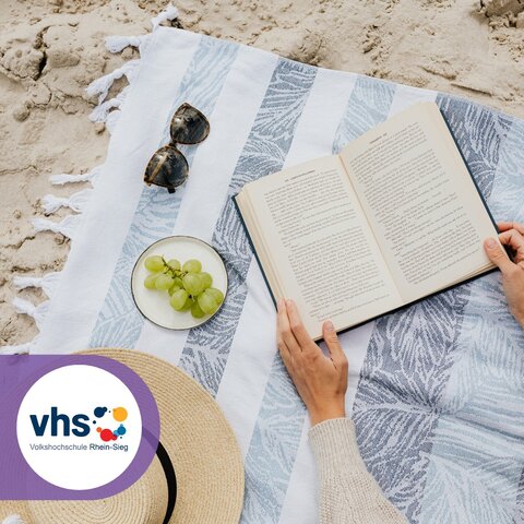 Frau liegt auf einer Decke am Strand und liest ein Buch.