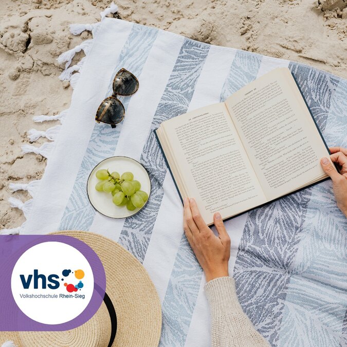 Frau liegt auf einer Decke am Strand und liest ein Buch.