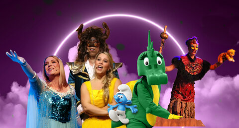 Bunte Bühnenaufnahme eines Familienmusicals mit mehreren kostümierten Darstellerinnen und Darstellern: eine Frau im glitzernden blauen Kleid, eine Sängerin im gelben Kleid, eine tierische Fantasiefigur mit Hörnern, ein grünes Drachenkostüm, eine kleine blaue Zeichentrickfigur sowie weitere märchenhafte Charaktere vor violett leuchtendem Hintergrund.