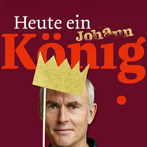 Porträt von Comedian Johann König vor dunkelrotem Hintergrund. Er hält eine goldene Papierkrone vor sein Gesicht. Über dem Bild steht in großer Schrift „Heute ein König“ mit seinem Namen „Johann“ darüber.