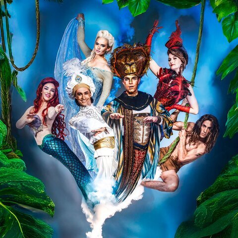 Eine fantasievolle, farbenprächtige Collage zeigt sechs märchenhafte Figuren, die aus blau-weißem Rauch einer goldenen Wunderlampe emporsteigen. Links eine Meerjungfrau mit rotem Haar und schillerndem türkisgrünem Fischschwanz. Daneben ein strahlender Mann in weißem orientalischem Gewand. In der Mitte steht eine imposante Figur mit goldener, kunstvoll verzierter Kopfbedeckung und prunkvollem Gewand. Rechts davon eine Frau in einem roten, federartigen Kostüm, die sich an einem Seil hält. Am oberen Rand schwebt eine elegante Frau in eisblauem Kleid mit heller Hochfrisur. Ganz rechts hält sich ein muskulöser Mann mit langen Haaren an einer Liane fest. Alles ist umrahmt von großen grünen Blättern, die eine magisch-dschungelartige Szene erzeugen.